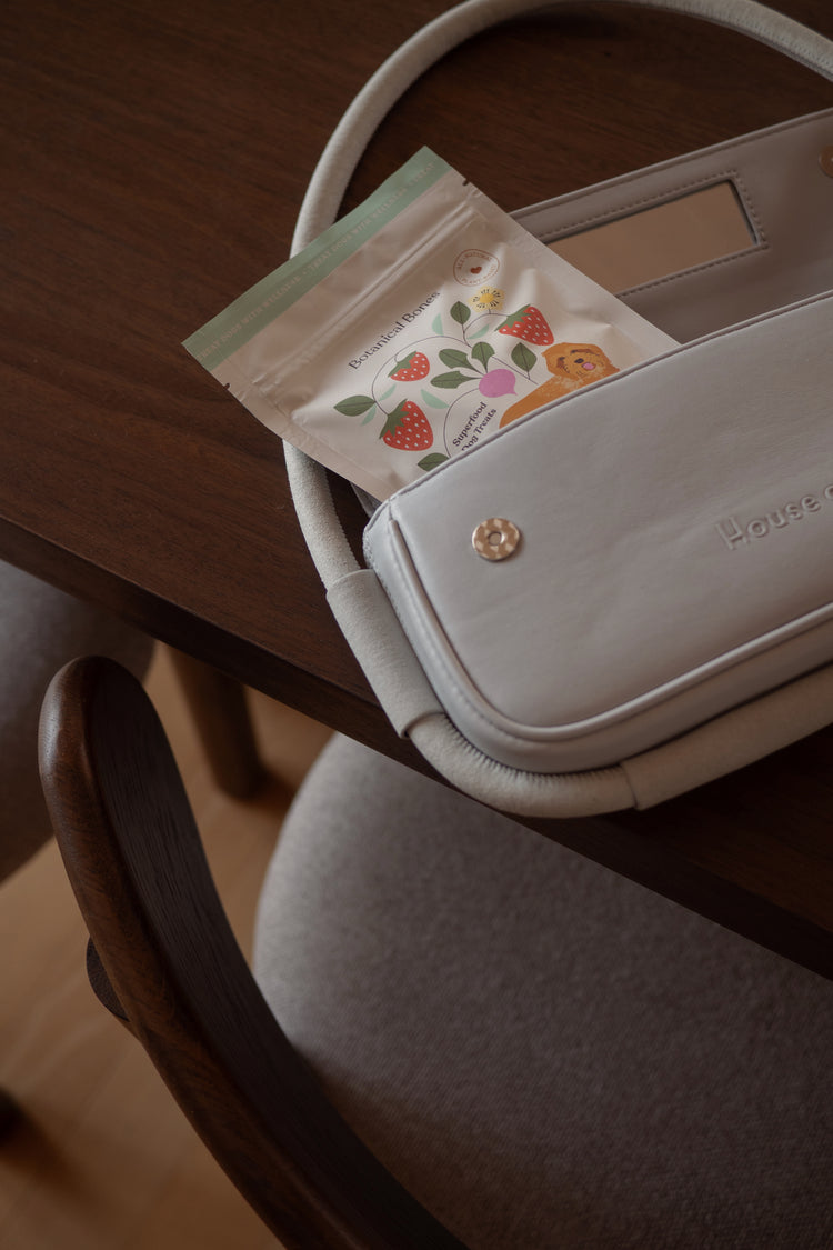 White handbag with a small pouch containing strawberry dog treats from Botanical bones items on a wooden surface.