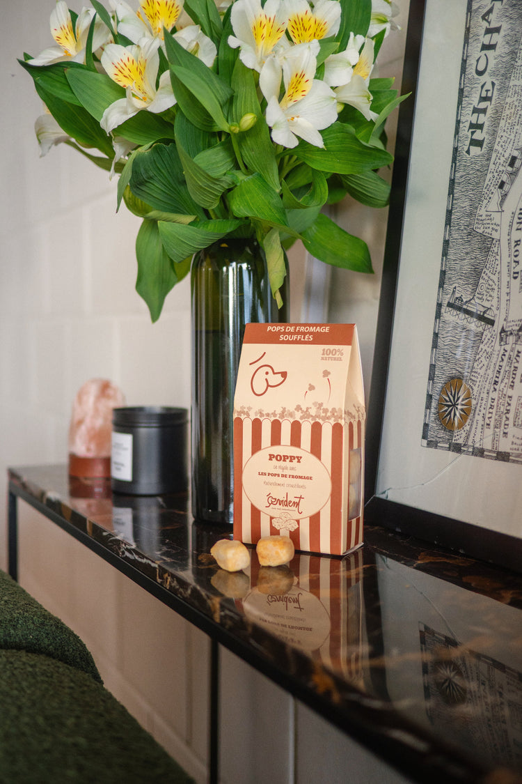 Bouquet of white flowers in a vase on a table with a box labeled 'Pops cheese' and decorative items.