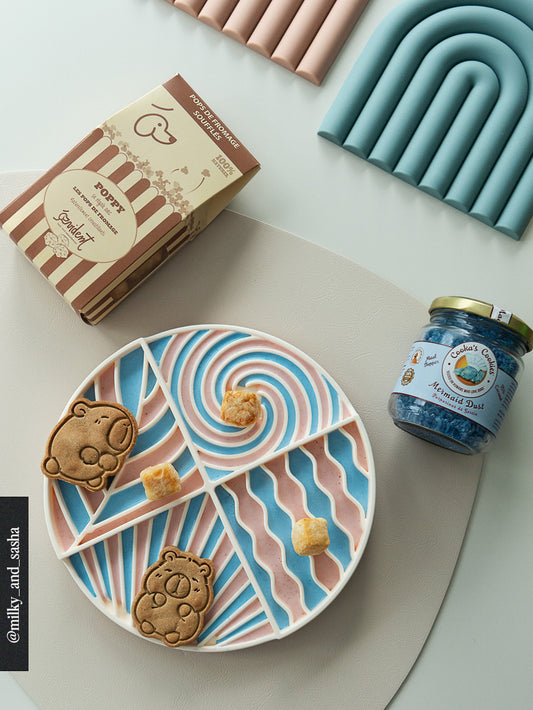 Colorful lick mat with bear-shaped cookies, a jar of jelly, and a box of Poppy cheese treats on a light background