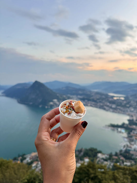 Hand holding a small cup with a Popincinno against a scenic backdrop of mountains and water.