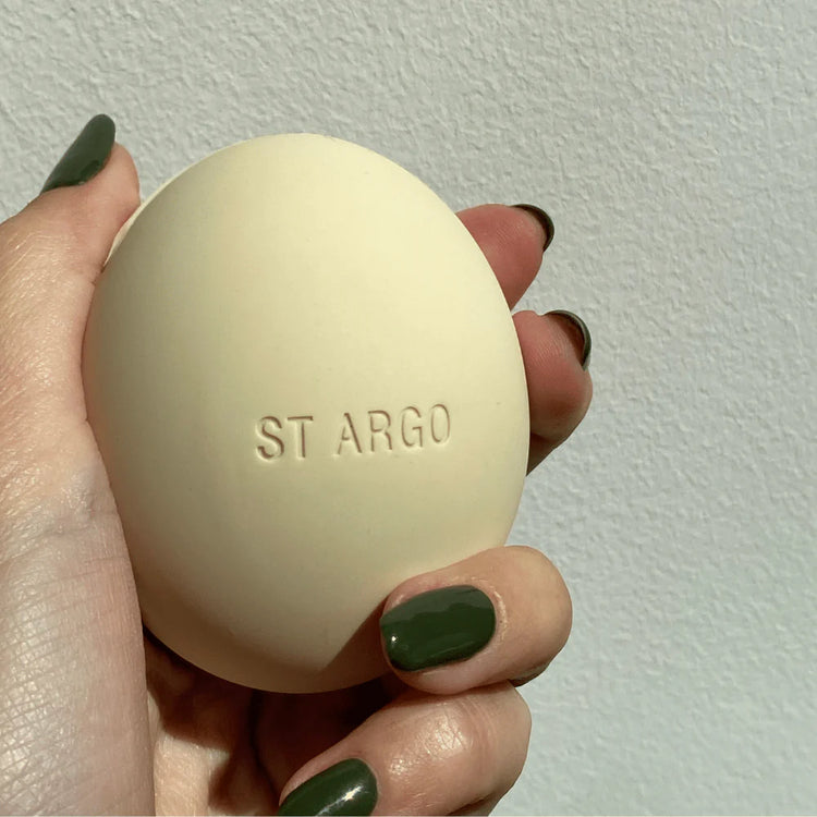 Hand holding a beige oval-shaped treat pouch with 'ST ARGO' branding against a light background