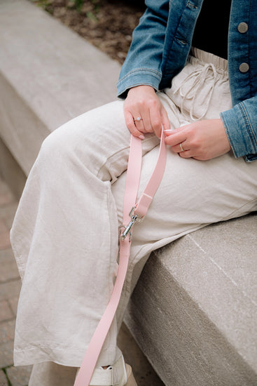 Person holding a pink dog leash, sitting on a stone bench.